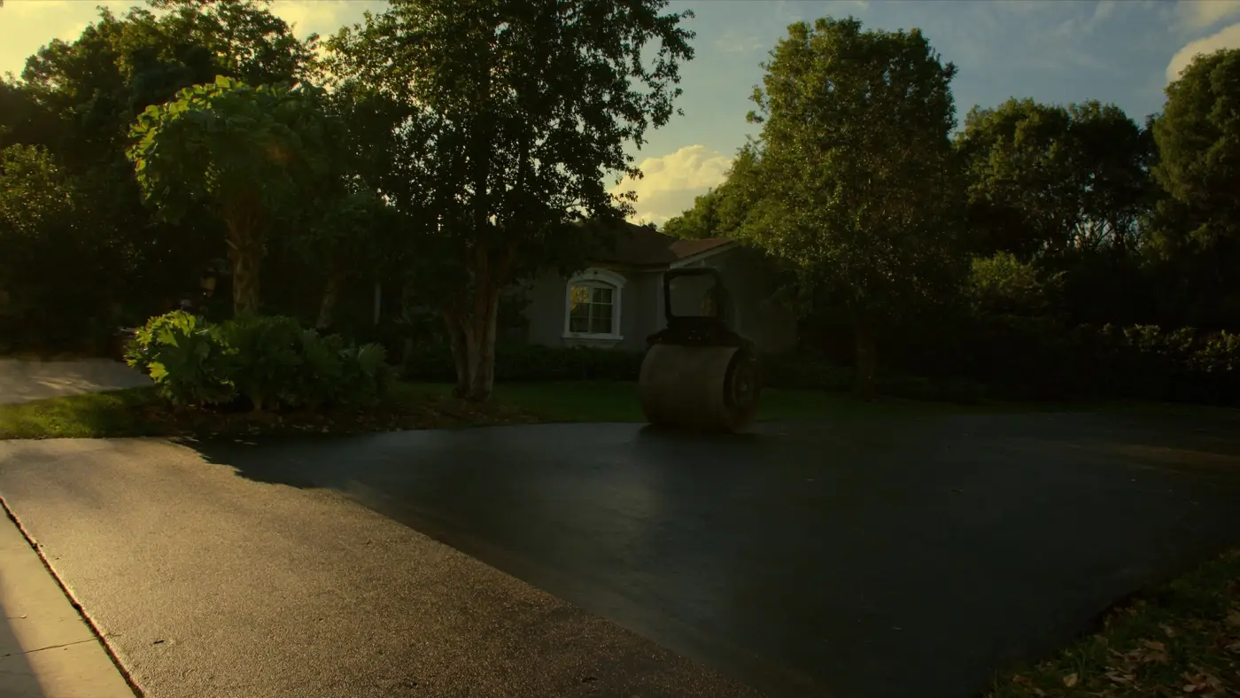 A fresh mat of black asphalt laid on a residential driveway with a steel roller behind it